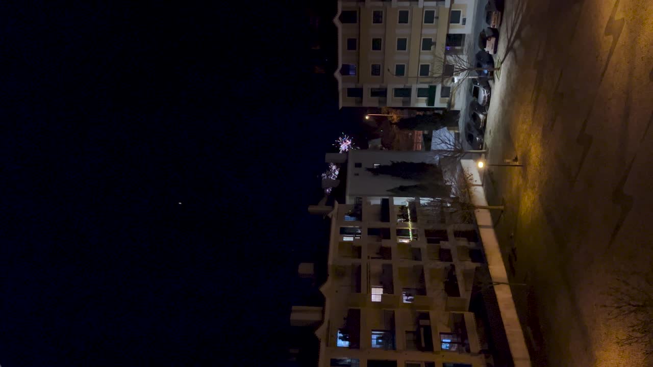 Vertical video of a residential building in Portugal with vibrant fireworks bursting in the night sky. Festive and celebratory scene. Perfect for holiday, celebration, and urban life content.