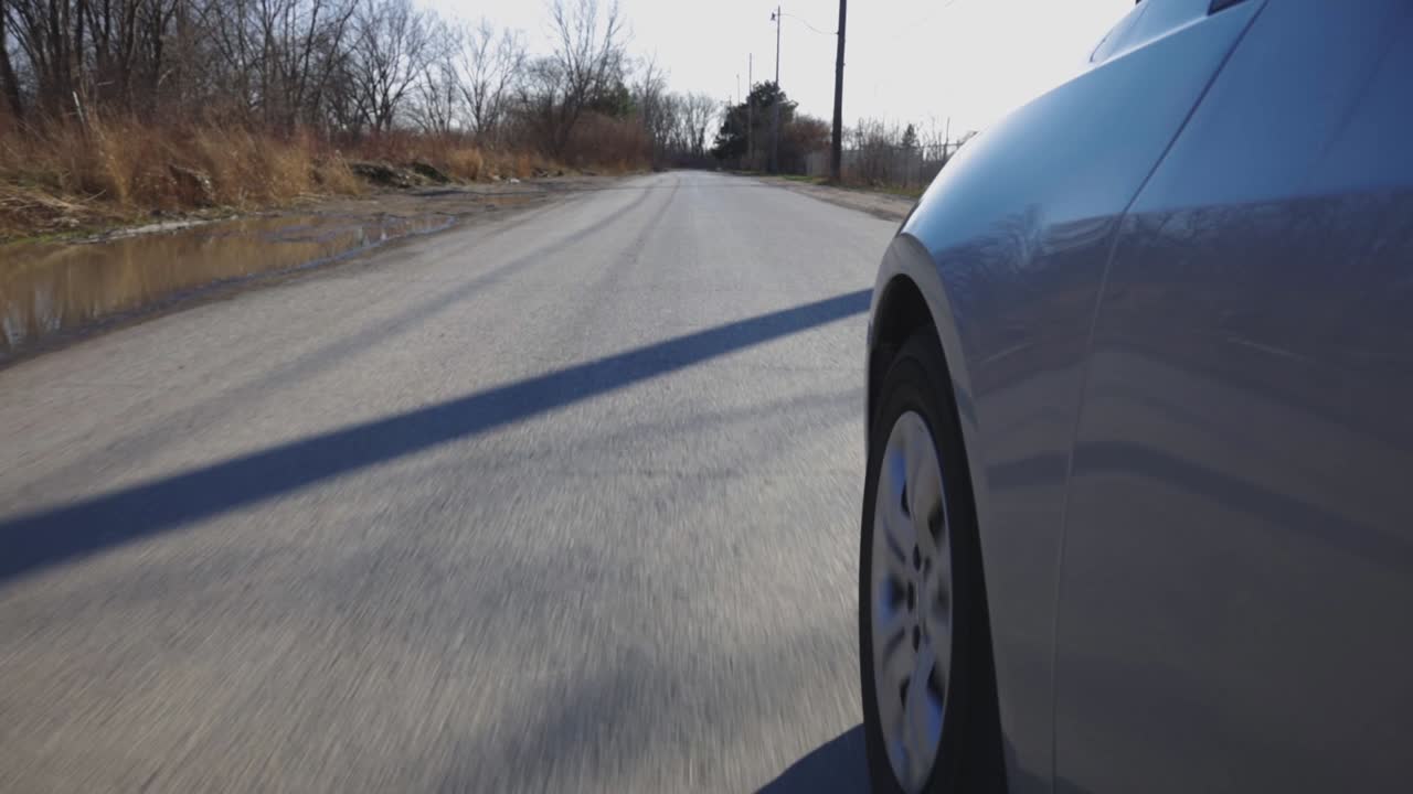 Left Front Wheel Of A Car Driving On The Asphalt Road On A Bright Weather - Closeup Shot