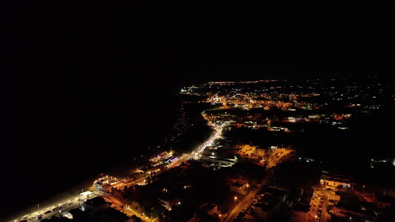 Stunning 4K drone footage of the sea at night, with illuminated coastline and city lights