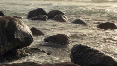 waves rolling and crashing into rocky shore in afternoon sun, slow motion