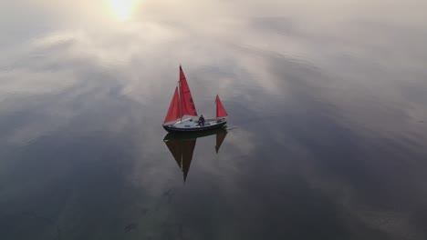 Sail-yacht-with-red-sails-at-Nationaal-Park-Lauwersmeer-during-sunrise,-aerial