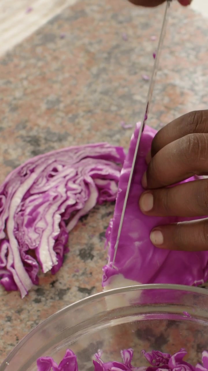 Vertical video: Pressing knife, hands slicing purple cabbage on counter at home into bowl for salad
