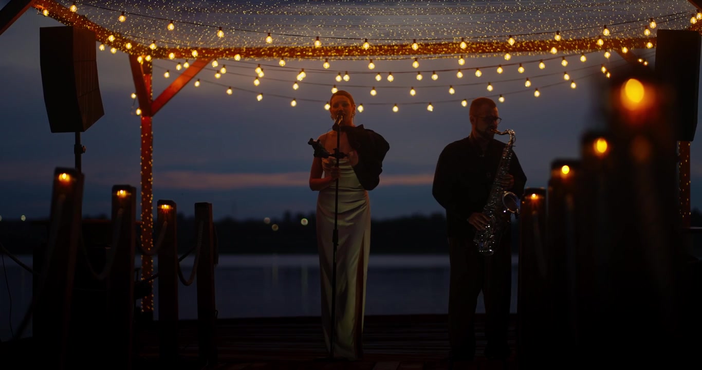 Female Singer and Saxophonist Performing on Outdoor Stage at Sunset