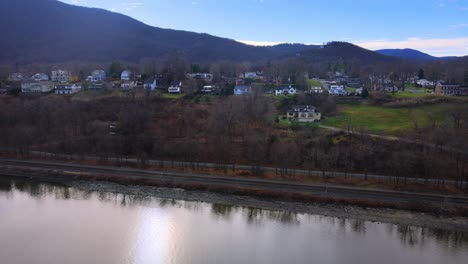 aerial footage panning sideways and rising up over a quaint smell town on a riverbank, with a mountain range in the background