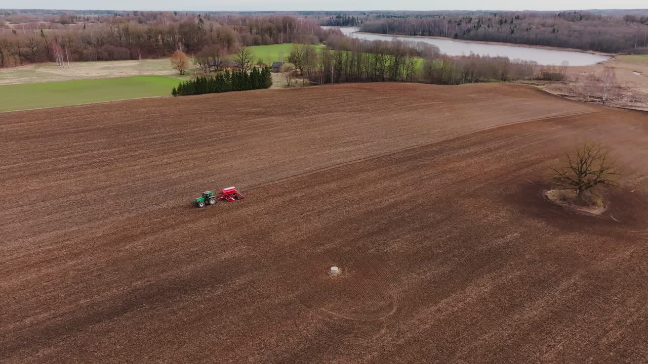 Jevn droneflyging viser traktor som sår avlinger over forberedt jordbruksåker