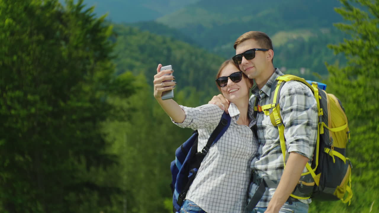 una pareja joven de turistas con mochilas se toman fotos con un teléfono inteligente en una hermosa
