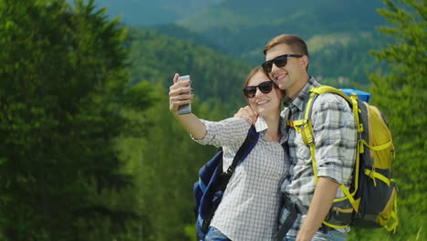 a young couple of tourists with backpacks take pictures of themselves with a smartphone on a beautif