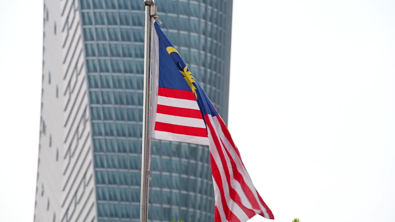 agitando la bandera de malasia en el fondo de un edificio de oficinas