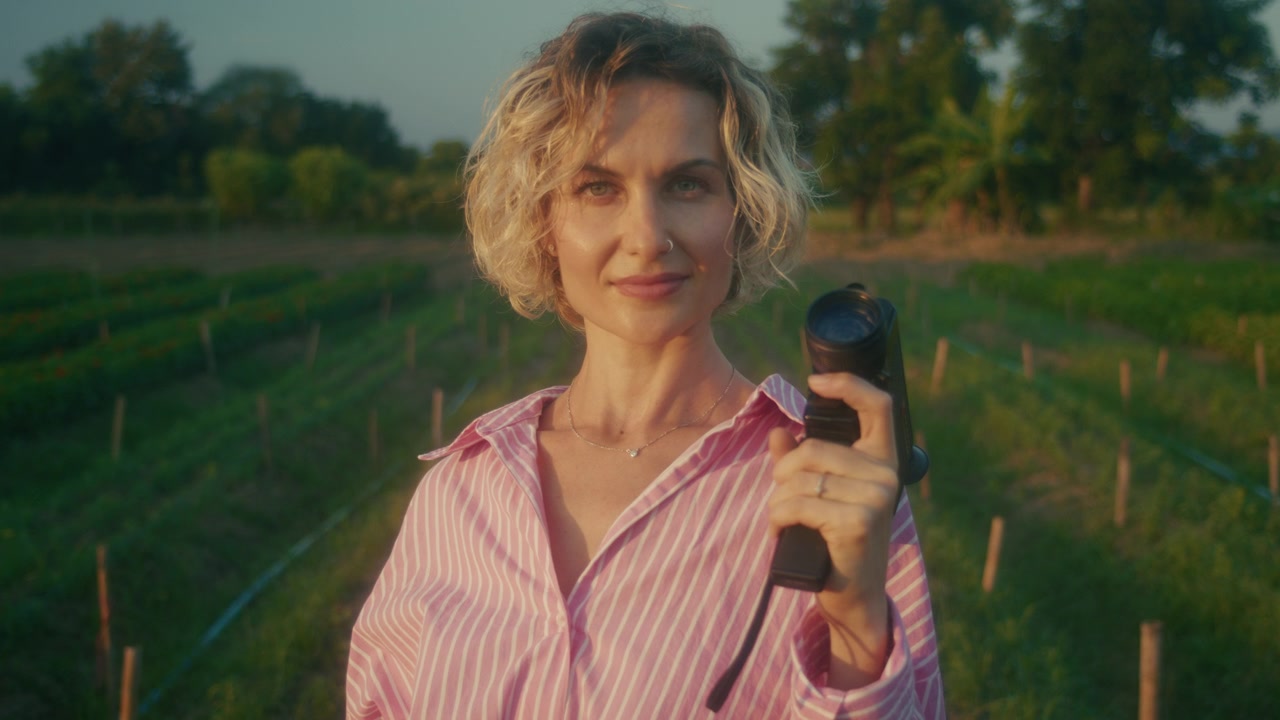 Female Farmer Holding Binoculars in Agricultural Field at Sunset