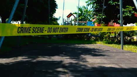 scary and sad low angle footage of yellow colored vibrant crime scene do not enter tape in front of two empty swings swinging at a playground showing that something has happened with a child. daytime.