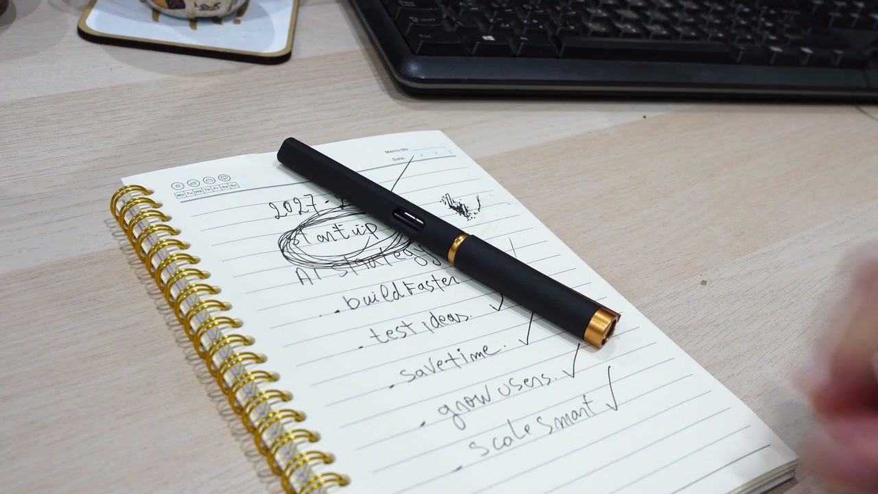 Close up shot of male hands holding a black pen over a spiral notebook with a handwritten startup strategy list. The worker evaluates the business goals at a modern indoor wooden office desk.