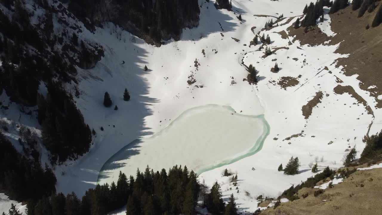 Drone flies over the frozen Walopsee and pans against the high snowy mountains in the background, sunny and clear (swiss alps)