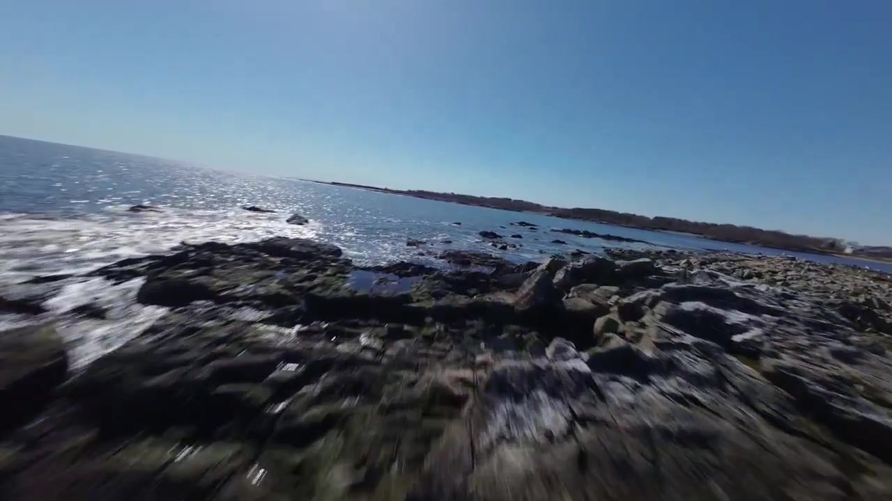 Imagem de drone FPV avança em direção a uma pequena massa de terra rochosa no meio do oceano, perto da costa acidentada de New Hampshire, EUA.