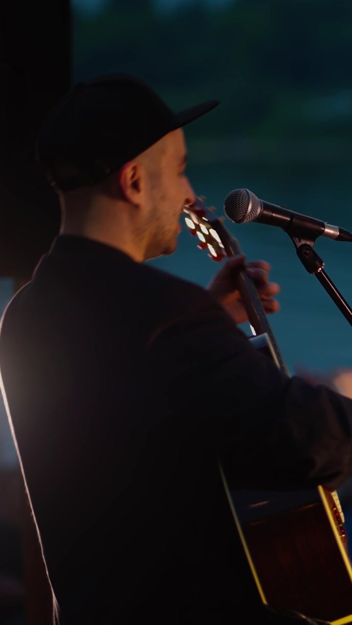 Mann synger og spiller akustisk gitar på scene om natten