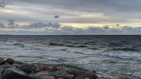 crashing waves on a rocky shore against cloudy sky with birds flying on a windy day during sunset