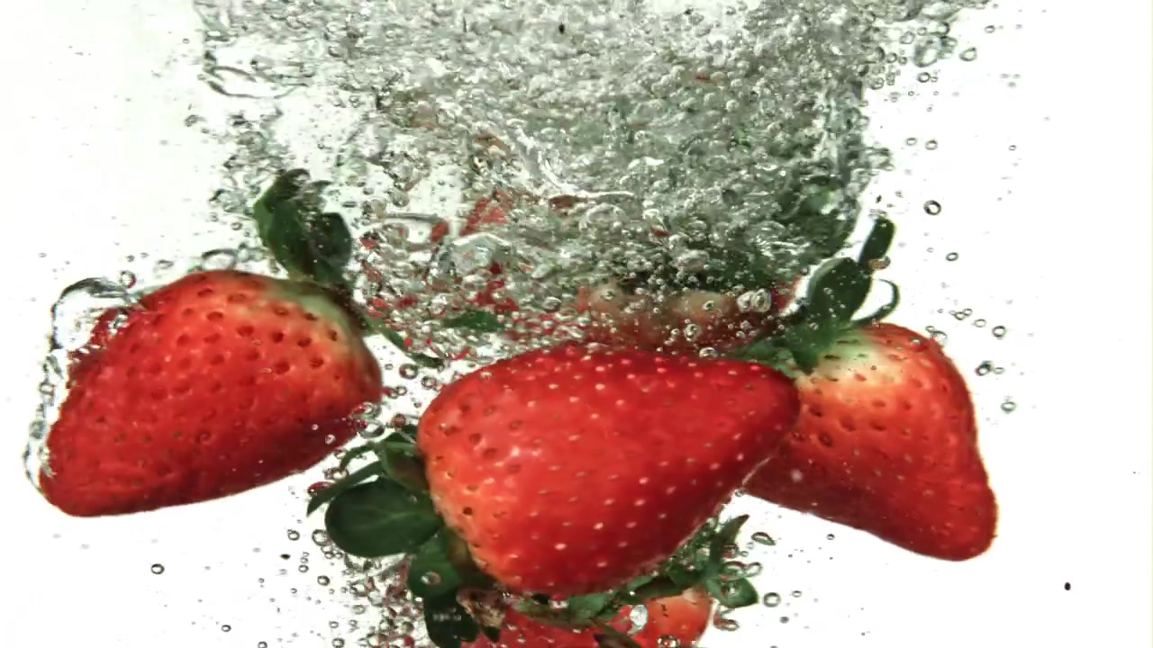 Fragole rosse fresche che si tuffano in acqua limpida al rallentatore