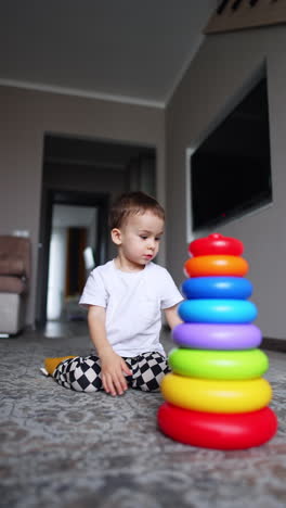 colorful pyramid is on the floor in the room. toddler runs up to the toy from another room. vertical video.
