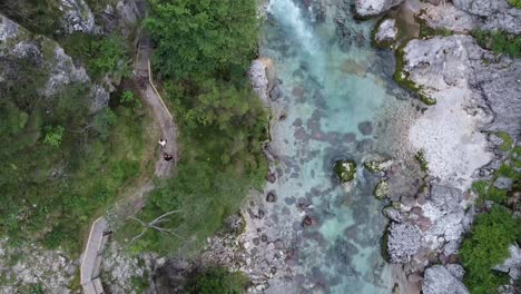 Fresh-water-of-Dolomites-river-with-people-walk-nearby-on-trekking-path,-top-down