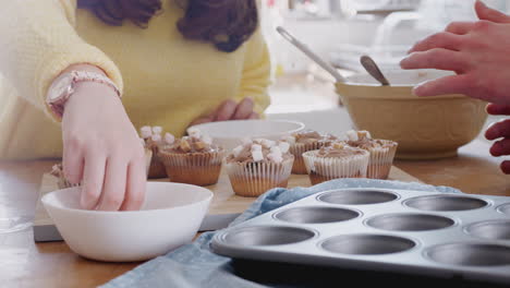 close up of downs syndrome couple decorating homemade cupcakes with marshmallows in kitchen at home