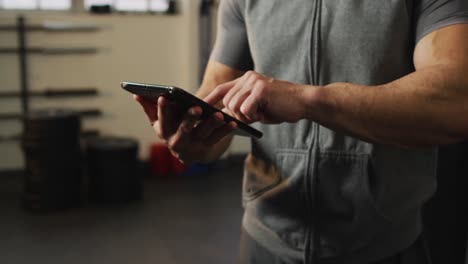 Sección-Media-De-Un-Hombre-Caucásico-En-Forma-Usando-Una-Tableta-Digital-En-El-Gimnasio