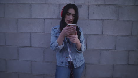 Young-woman-happy-listening-music-in-a-wall-wearing-red-headphones