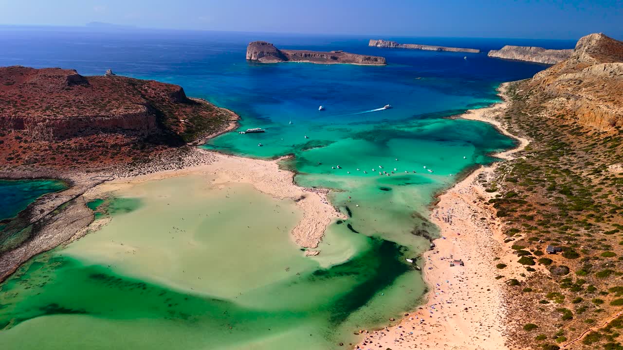 Gaze at the breathtaking beauty of the coastline in Crete, featuring clear turquoise waters, sandy beaches, and rocky formations under a bright blue sky