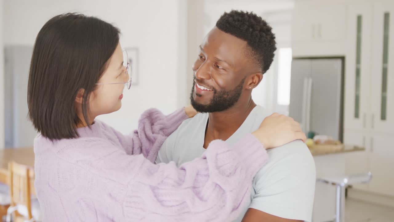 Happy diverse couple embracing, looking in eyes and dancing in kitchen