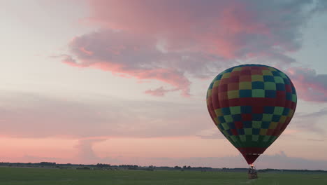 passenger drifting smoothly in hot air balloon across farm land under pink and blue sky at dusk with burner flame pulsing beneath colorful clouds reflecting evening light on tranquil countryside