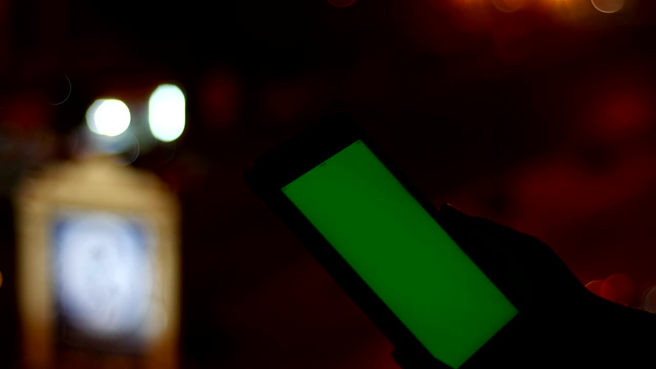 교통 신호등의 초점을 잃은 밤에 녹색 화면 태블릿을 사용하는 사람