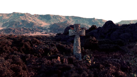 stone cross in a field with mountains in the background