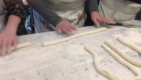 detail shot of group of various people rolling out pasta dough by hand on a marble countertop