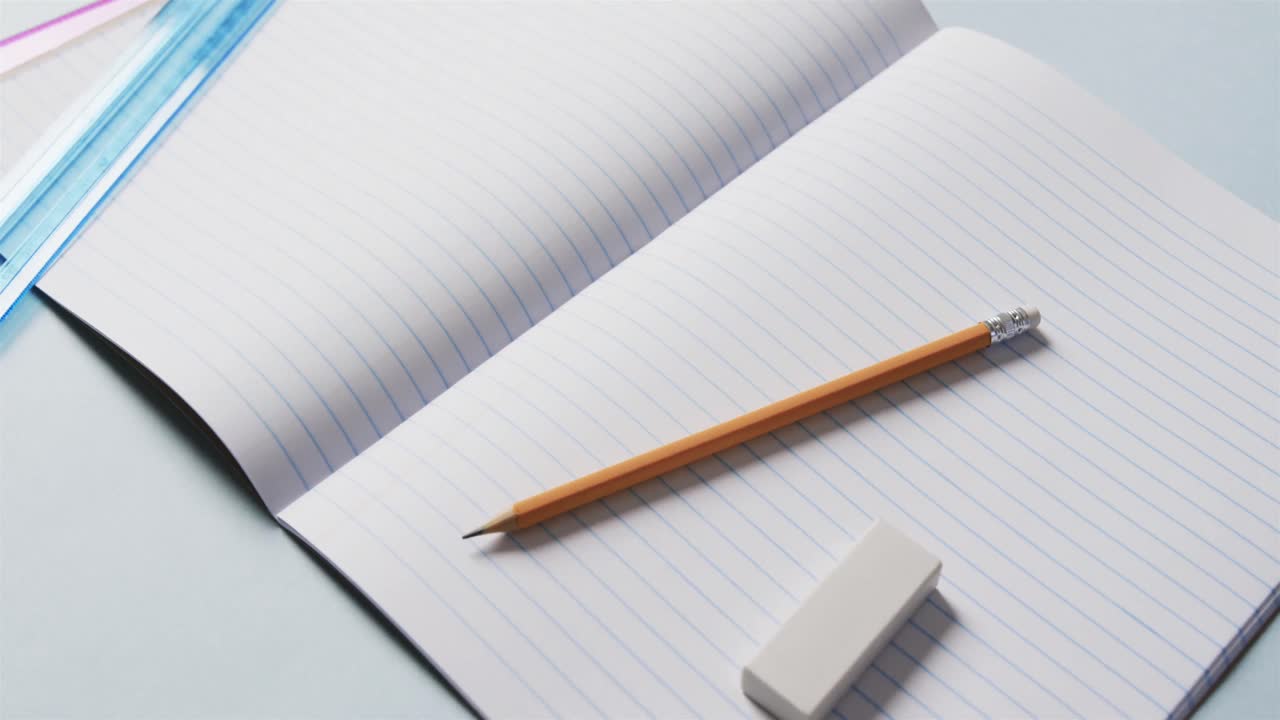 Close up of open notebook with school stationery on blue background, in slow motion