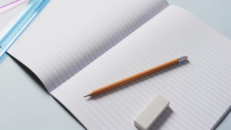 Close-up-of-open-notebook-with-school-stationery-on-blue-background,-in-slow-motion