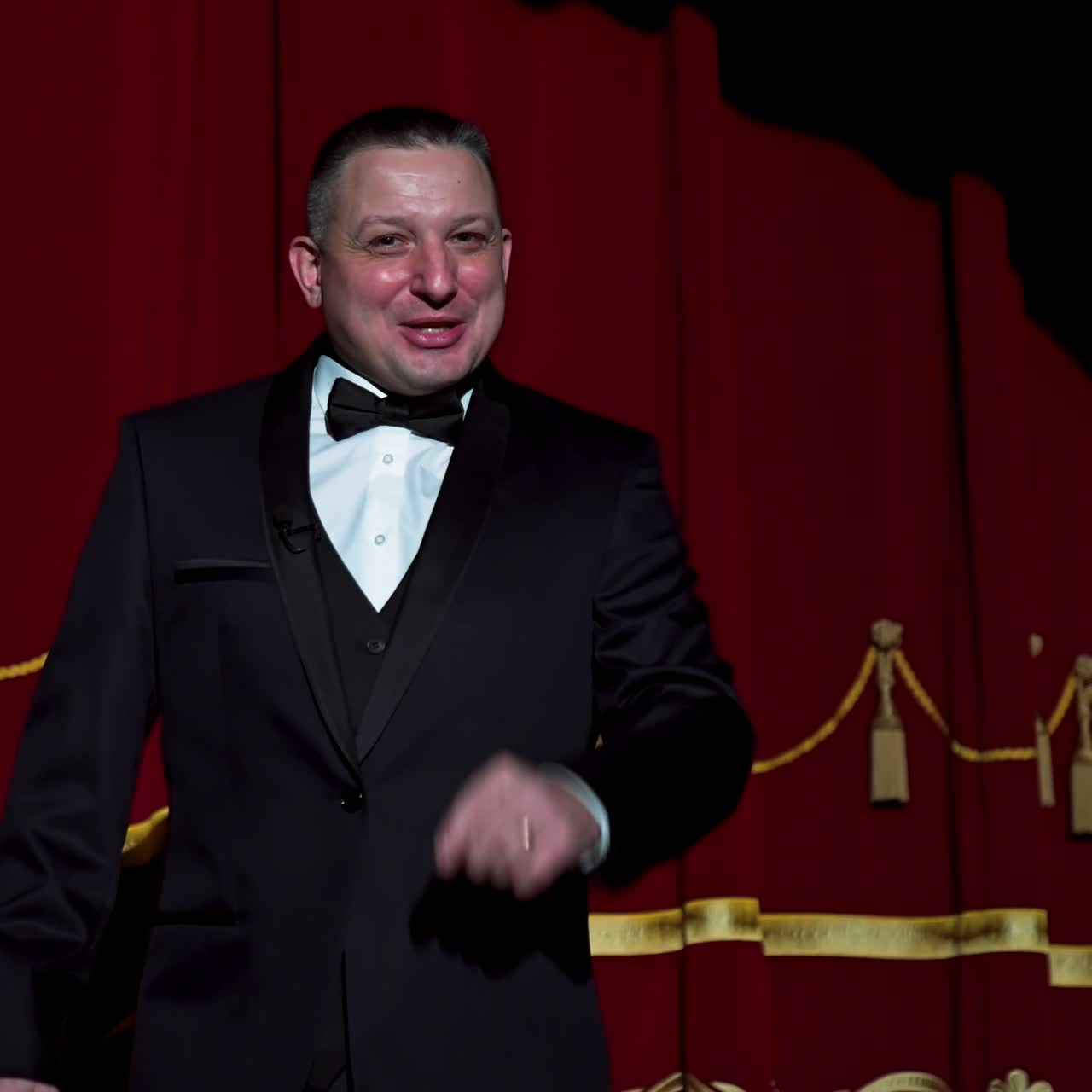 Portrait of a host. Man actor in black costume appears on stage and begins the speech in bright light spot in the theater