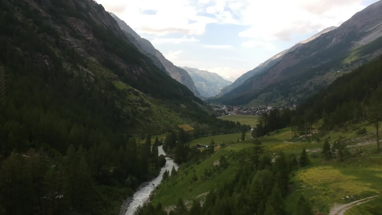 Paesaggio panoramico di valle montana con fiume e villaggio in lontananza.