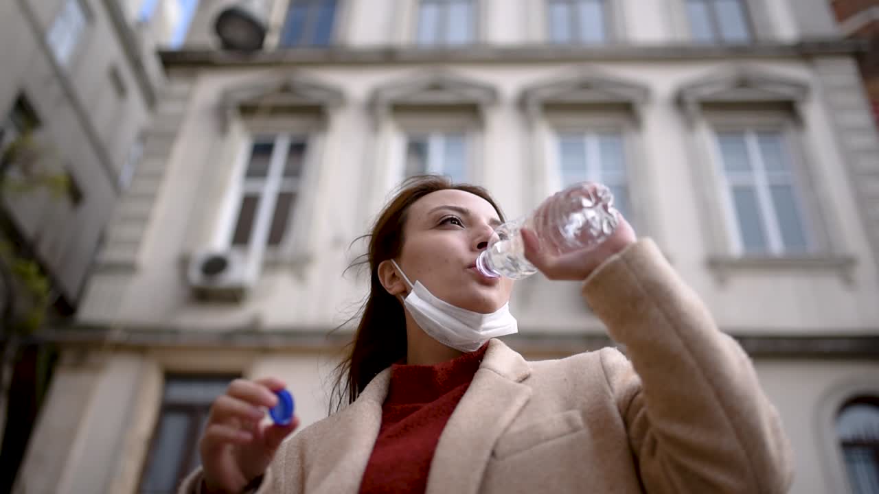 보호용 의료용 마스크와 세련된 옷을 입은 아름다운 소녀가 병으로 물을 마신다
