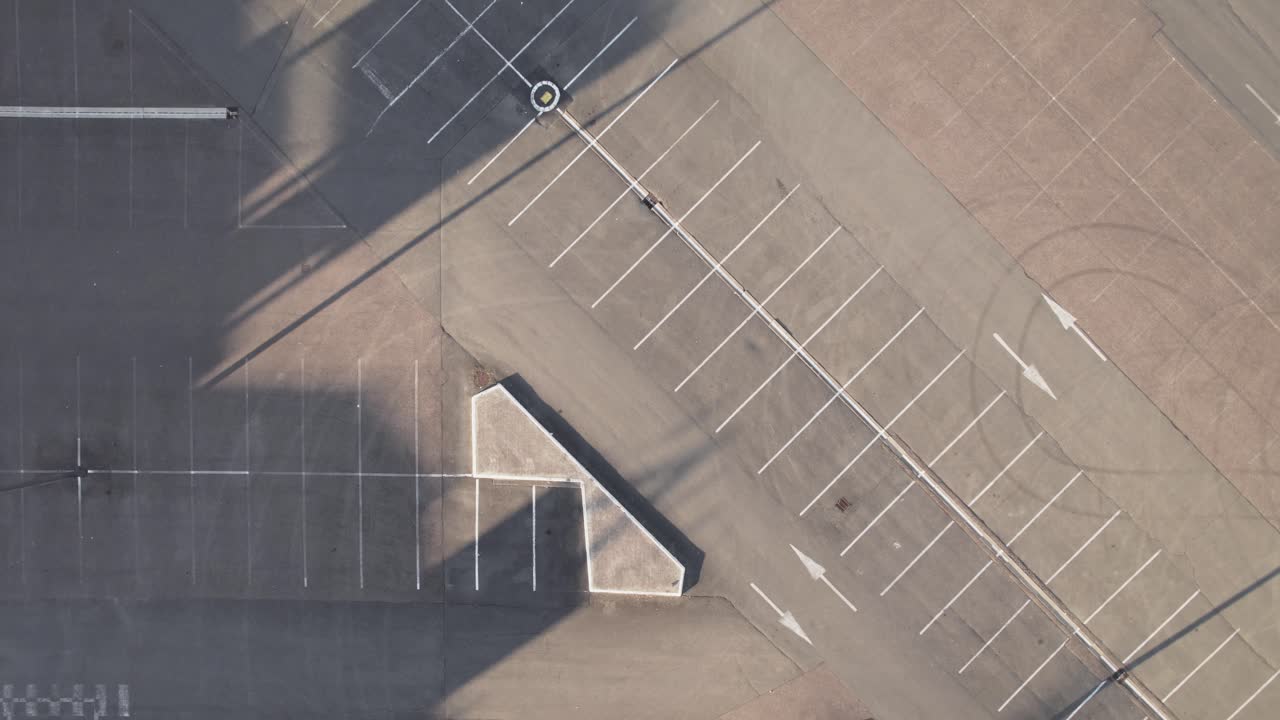 Empty asphalt parking lot with white lines and tire marks, aerial top down ascend and spin view