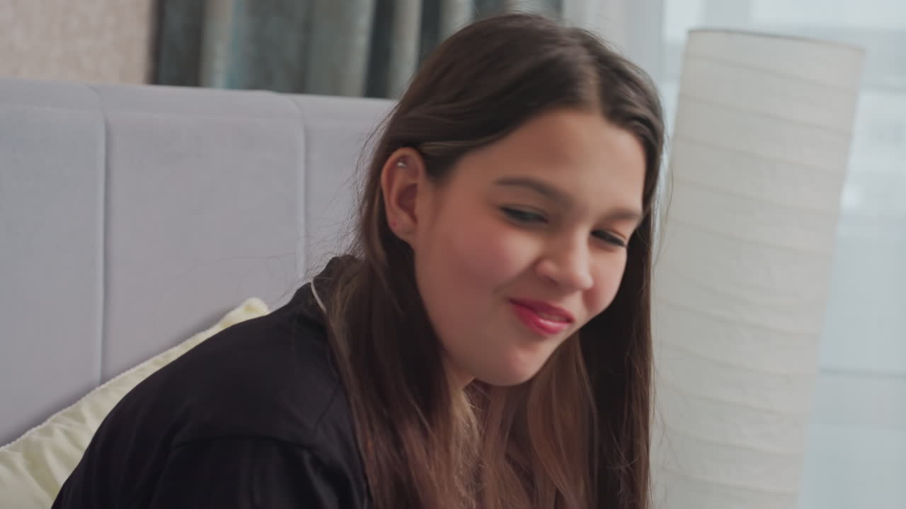 Close up of young woman enjoying sandwich while sipping hot tea, engaged in casual conversation, she sits on bed in relaxed setting, bathed in soft natural light from nearby window