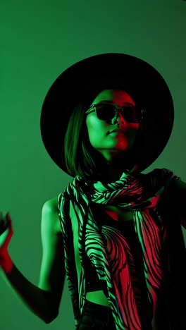 stylish woman in hat and sunglasses under neon green and red lights