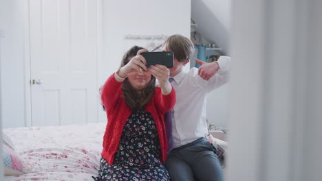 Loving-Young-Downs-Syndrome-Couple-Sitting-On-Bed-Using-Mobile-Phone-To-Take-Selfie-At-Home
