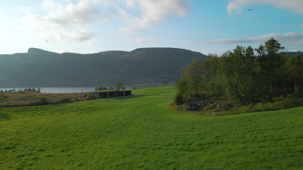 Grøn gård med traditionel landbrugsbygning i norsk landskab