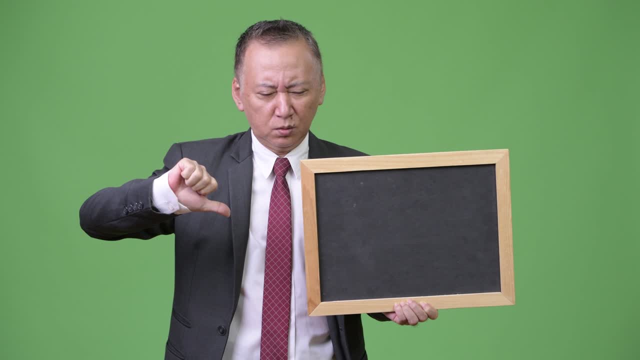 성숙 한 일본인 사업가 가 초록색 배경 에 검은판 을 들고 있다