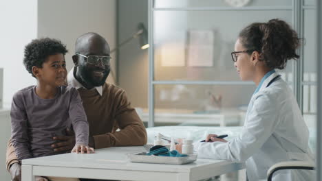 african american boy sitting with dad on consultation with female pediatrician