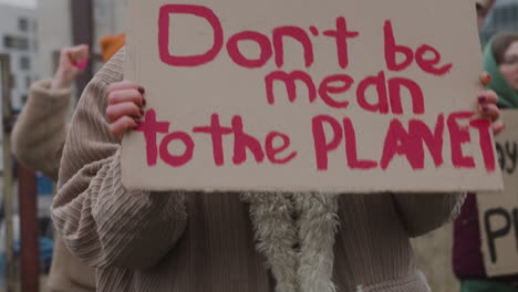 Nahaufnahme-Eines-Pappplakats-Mit-Der-Phase-Sei-Nicht-Gemein,-Der-Planet,-Der-Von-Einer-Frau-Während-Eines-Protestes-Gegen-Den-Klimawandel-Gehalten-Wird