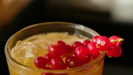 blue berries being dropped in yellow cocktail, next to red currant berries