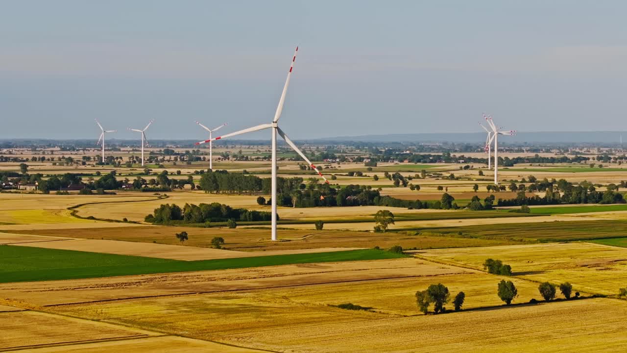 Rotating wind turbines tower above glowing Polish fields in golden hour light