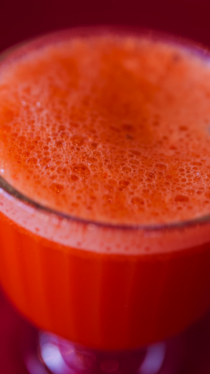 Primo piano di un succo di carota e arancia in un bicchiere con una cannuccia nera su una tovaglia rossa. Verticale