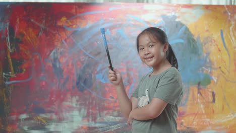 girl holding paintbrush in front of painting