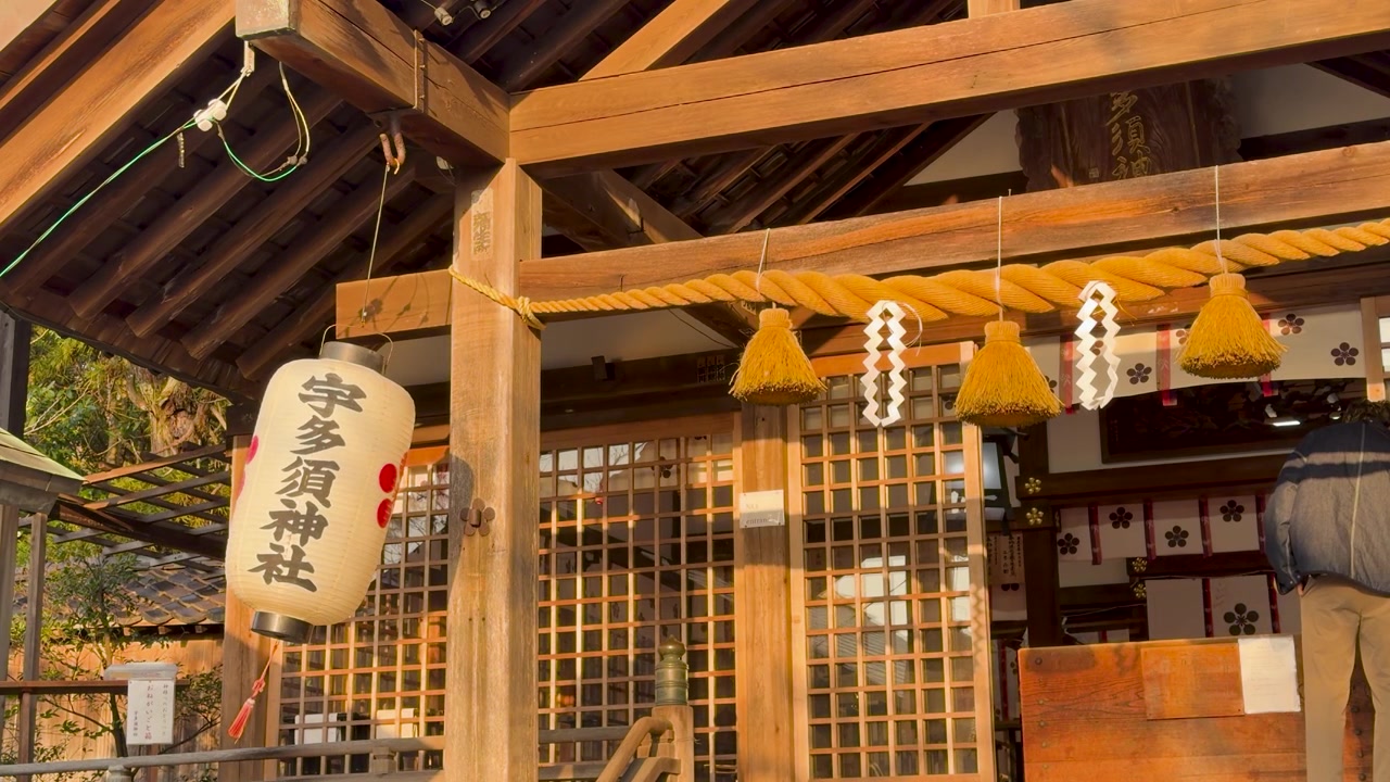 Golden hour sunlight illuminates the wooden facade, paper lanterns, and shimenawa rope of Utasu Shrine