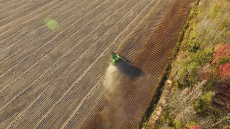 aerial view of a farm combine as it cuts corn stalks and piles chaff for the baling machine following behind. tracking on tractor as dust billows from behind. forward motion.